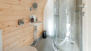 Un baño moderno con paredes de paneles de madera, un lavamanos blanco, un espejo y una ducha con mampara de vidrio.
