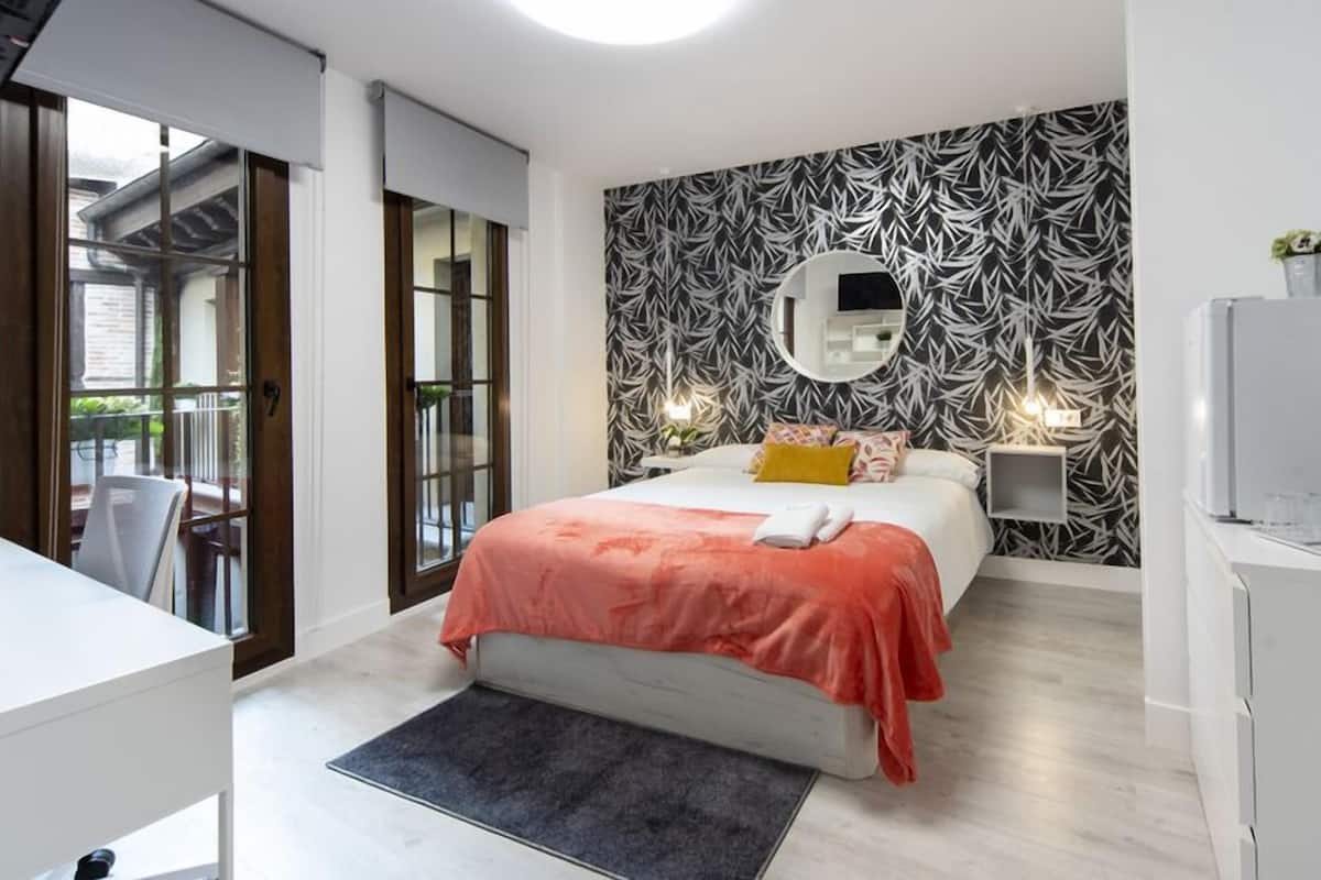 A modern bedroom with a bed, bedside tables, a desk, and a view through a glass door.