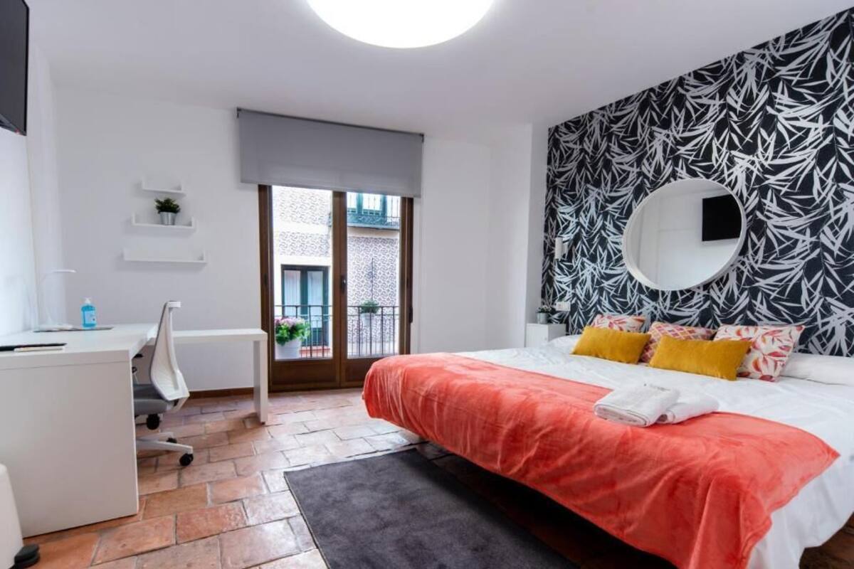 A modern bedroom with a large bed, a desk, and a balcony view.