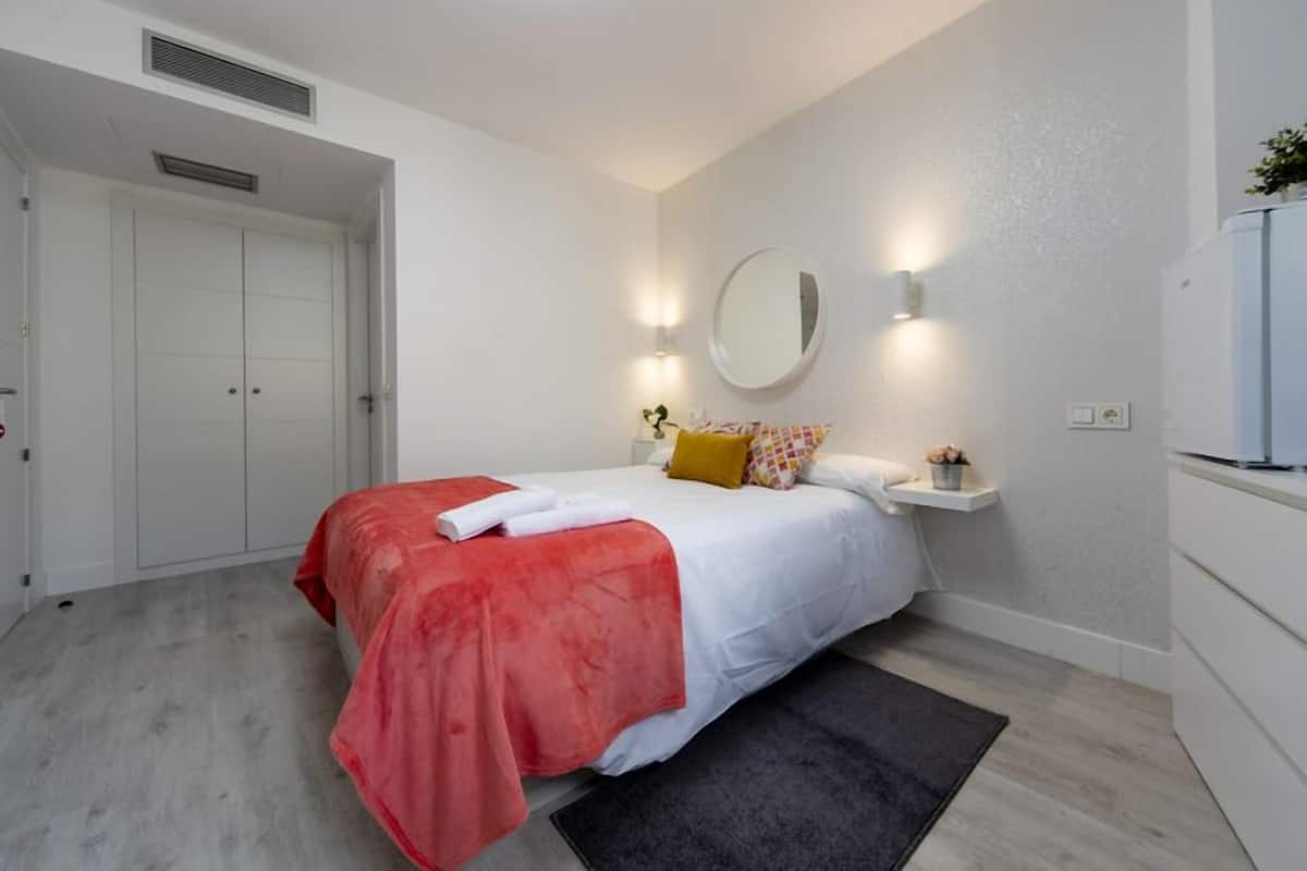 A bedroom with a bed, a bedside table, a mirror, and a wardrobe.