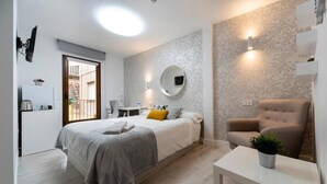 A modern bedroom with a bed, bedside table, chair, and a small table with a plant. - Vizcainos Home Away (Segovia)