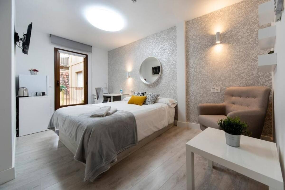 A modern bedroom with a bed, bedside table, chair, and a small table with a plant.