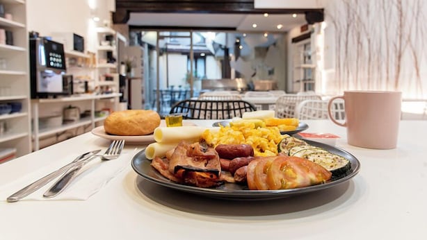 A breakfast plate with eggs, sausages, bacon, and toast on a table in a modern hotel room with a view of the city. - Vizcainos Home Away (Segovia)