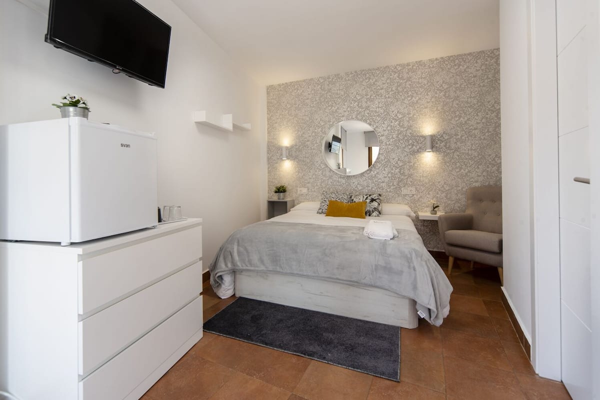 A bedroom with a bed, a dresser, a TV, a mirror, and a chair.