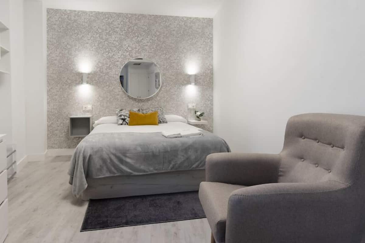 A modern bedroom with a bed, bedside tables, a chair, and a large mirror on the wall.