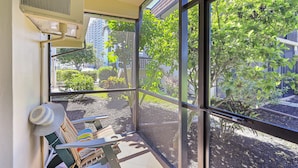 A balcony with a view of a garden and buildings, a sunshade, and a chair.