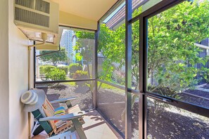 A balcony with a view of a garden and buildings, a sunshade, and a chair. - Quaint Condo | Steps to the Beach and Dining (Marco Island)