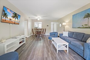 Una sala de estar con televisor, un sofá, una mesa de centro y un comedor con sillas y una mesa.