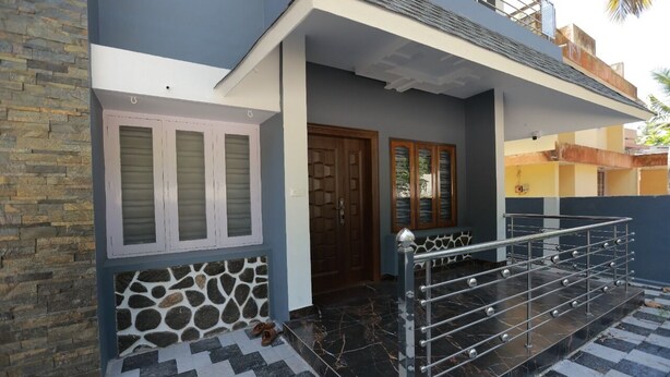 A modern two-story house with a stone facade, a tiled entrance, and a metal railing on the porch.