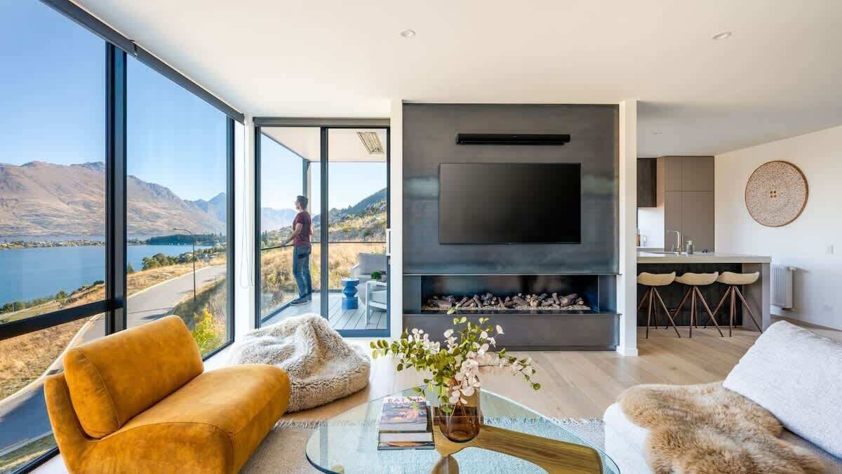 Uma sala de estar moderna com uma televisão grande, assentos confortáveis e vista para um lago e montanhas.