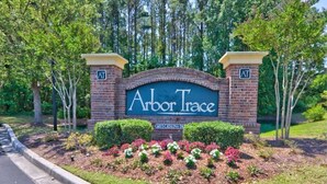 Señal de Arbor Trace con un arco de ladrillo y un área ajardinada con flores.