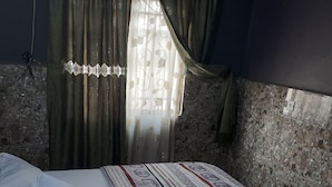 A bedroom with a bed, green curtains, and a window with a decorative curtain. - Sunrise hotels  (Owerri)