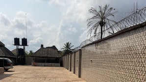 A paved courtyard with a brick wall, water tanks, and a thatched-roof building. - Sunrise hotels  (Owerri)