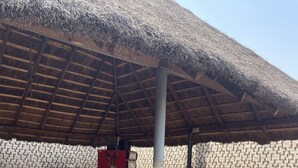 An outdoor seating area with tables and chairs, a thatched roof, and a patterned wall. - Sunrise hotels  (Owerri)