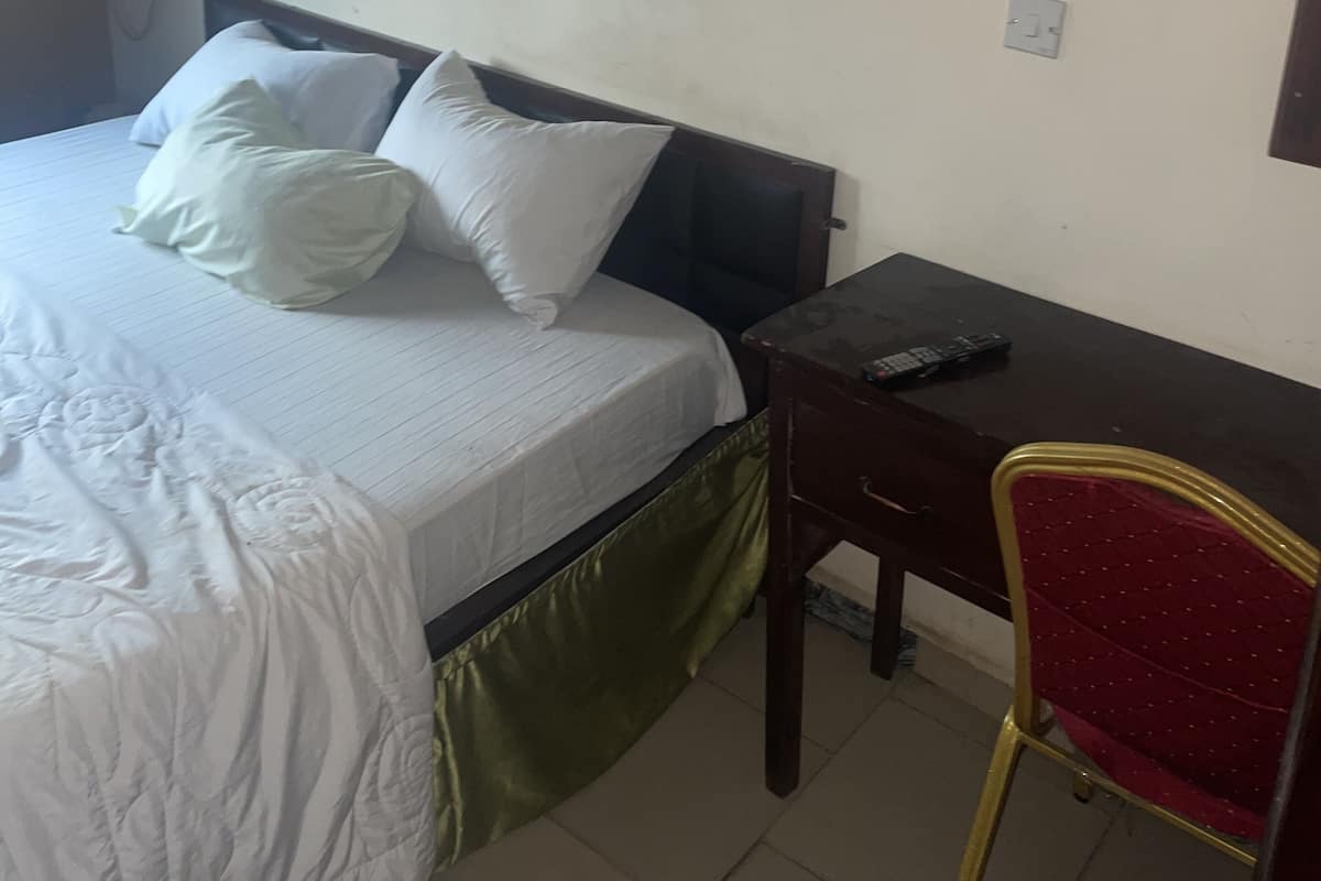 A hotel room with a bed, a desk, a chair, and a wall-mounted air conditioning unit.