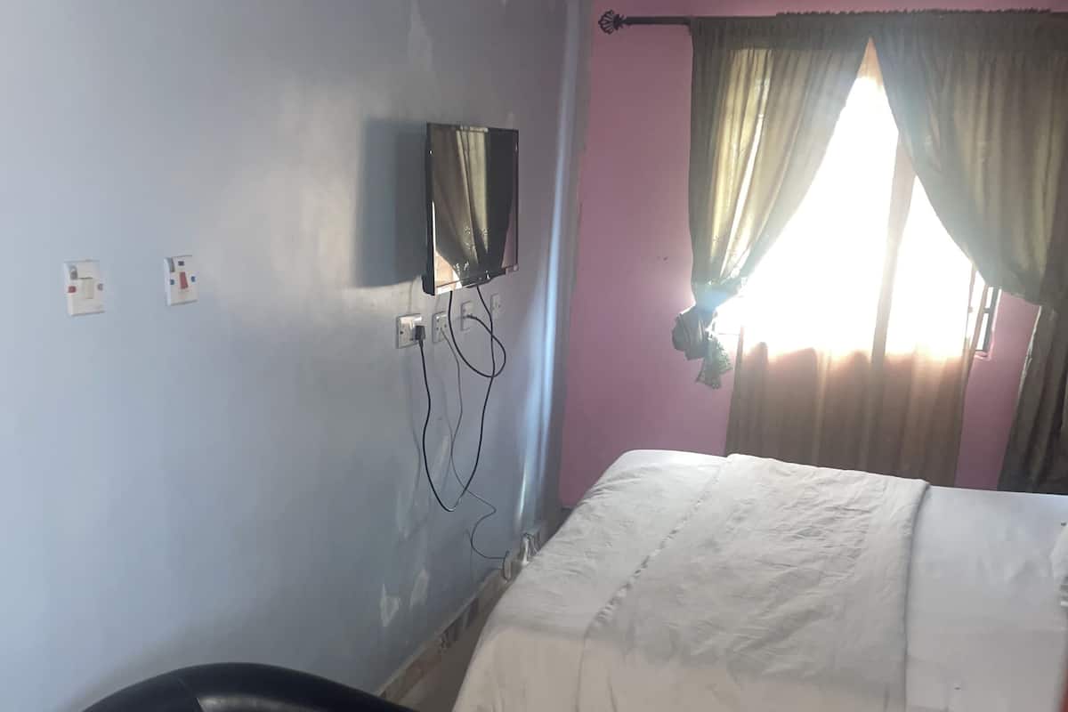 A room with a bed, a black chair, a wall-mounted TV, and a window with curtains.