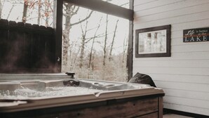 Ein Whirlpool mit Holzunterbau, beschriftet mit "Viking Spa", ein Fenster mit Blick auf Bäume und ein Wandschild mit der Aufschrift "Das Leben ist besser am SEE".