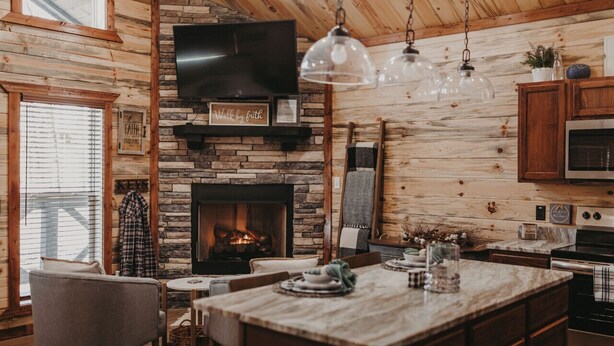 Ein gemütliches Blockhaus-Interieur mit Kamin aus Stein, Holzwänden, einer Essecke und einer Küche mit Mikrowelle und Herd.