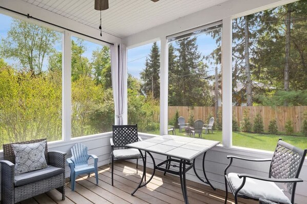 Une terrasse couverte avec une table et des chaises, de grandes fenêtres et une vue sur le jardin.