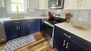 A modern kitchen with dark blue cabinets, a stainless steel range, and a microwave above the stove. - Westerly Retreat (Westerly)