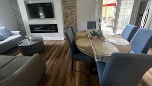 A modern living room with a flat-screen TV mounted on the wall, a dining area with blue chairs and a wooden table, and a stone accent wall. - Westerly Retreat (Westerly)