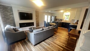 A modern living room with a grey sectional sofa, a flat-screen TV mounted on the wall, and a dining area with a wooden table and chairs. - Westerly Retreat (Westerly)