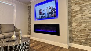 A modern living room with a flat-screen TV mounted on the wall, a fireplace below it, and a round coffee table with a remote control on it. - Westerly Retreat (Westerly)