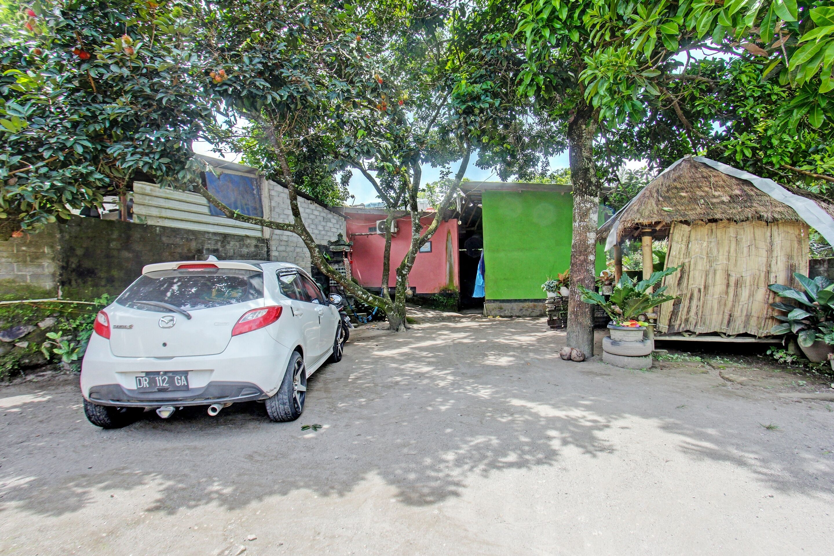 A white car parked in a driveway with a house and a small hut in the background.