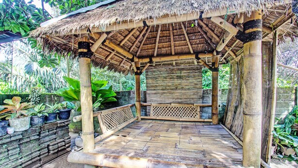 A bamboo structure with a thatched roof, surrounded by lush greenery and potted plants.