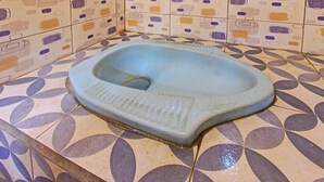 A small, square-shaped toilet with a simple design, situated in a corner of a bathroom with patterned tiles.
