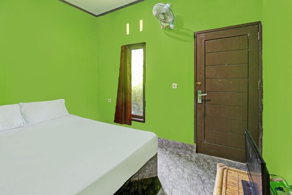 Una habitación con cama, puerta, ventana con cortinas y un ventilador en la pared.