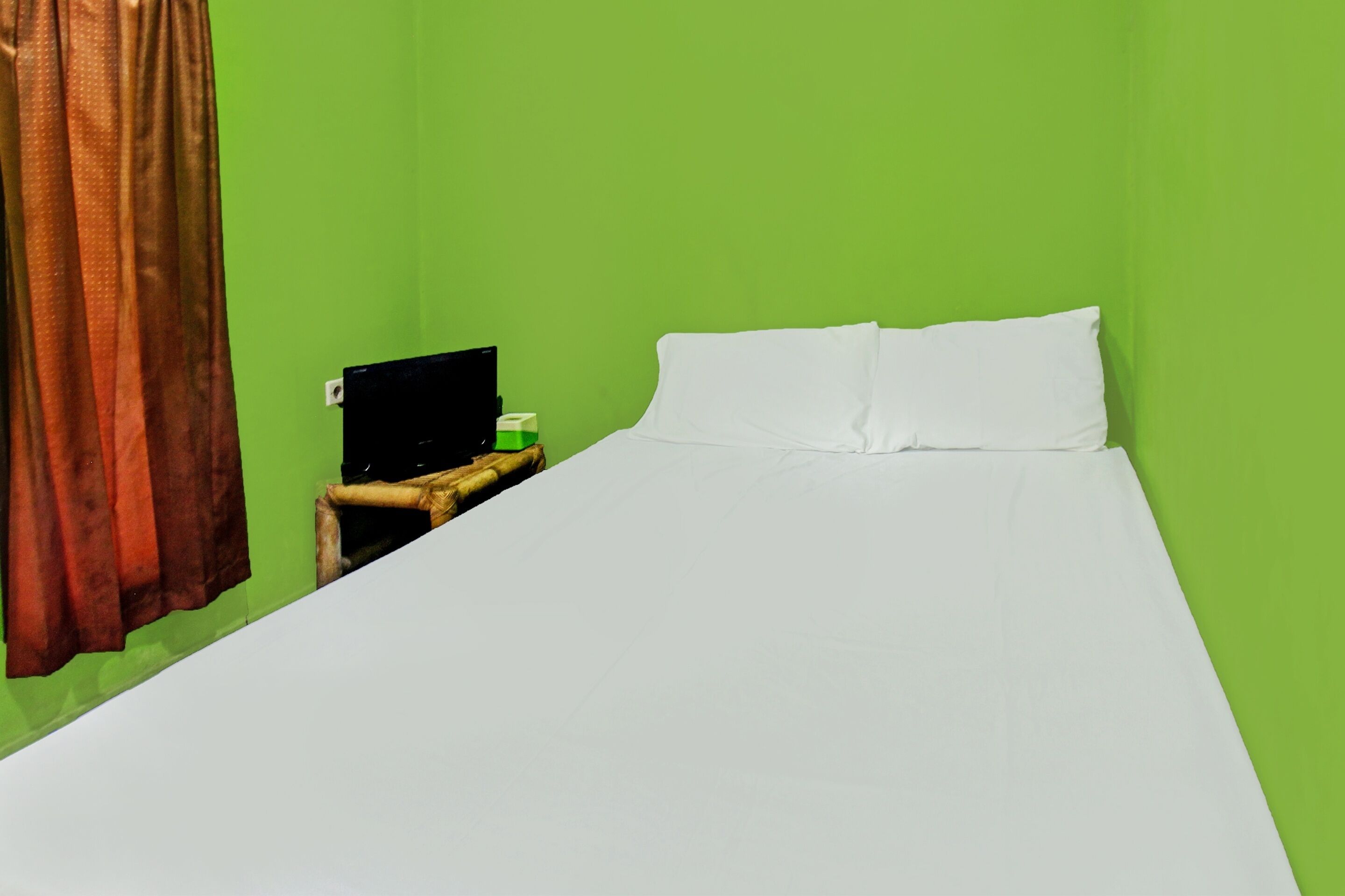 A single bed with white bedding in a room with green walls.