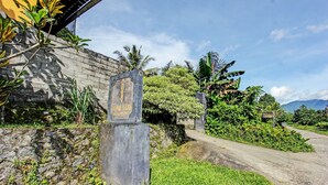 A stone wall with a sign that reads "HOME STAY" and a road leading into a lush, green area with mountains in the background.