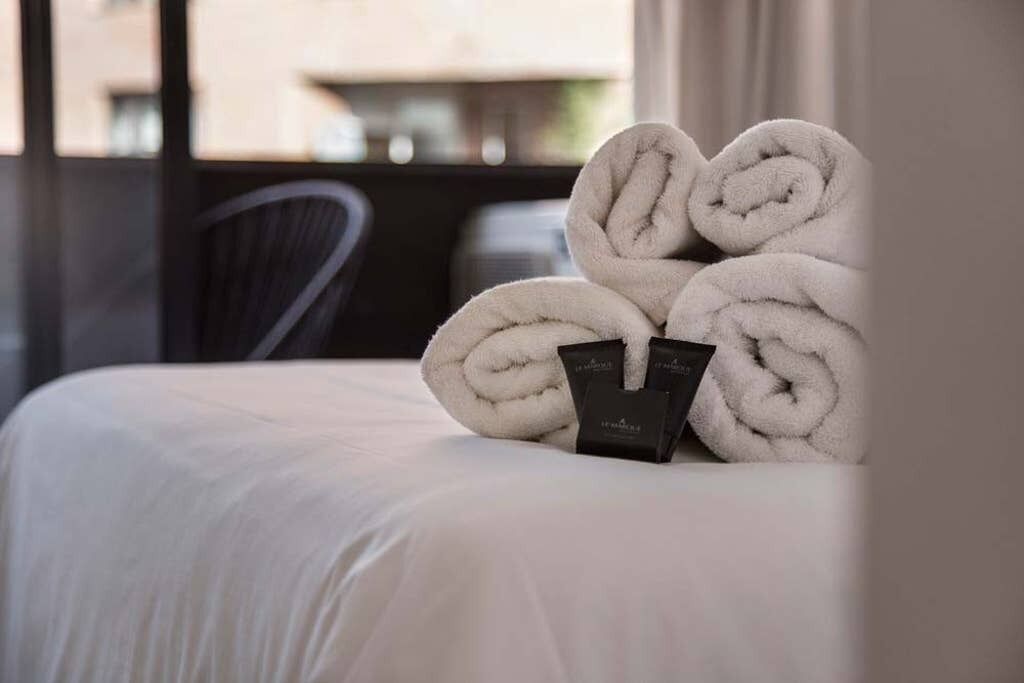 Een net opgemaakt bed met opgerolde witte handdoeken en een zwarte kaart erop.