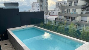 A rectangular swimming pool with clear blue water, surrounded by a tiled deck and a low wall. - Luminous apt 4ppl Palermo Soho (Buenos Aires)