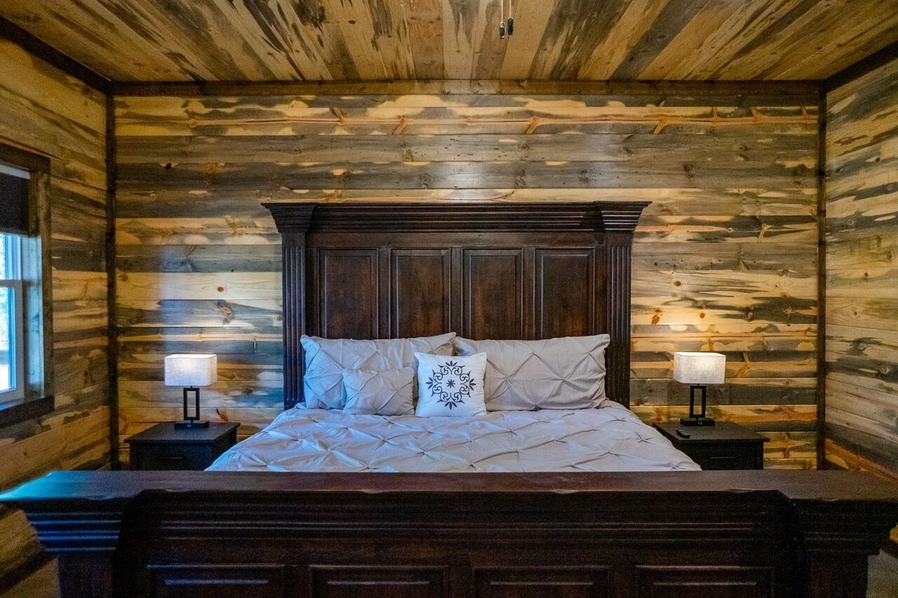 Un dormitorio con paneles de madera, una cama grande, dos lámparas de noche y un ventanal.