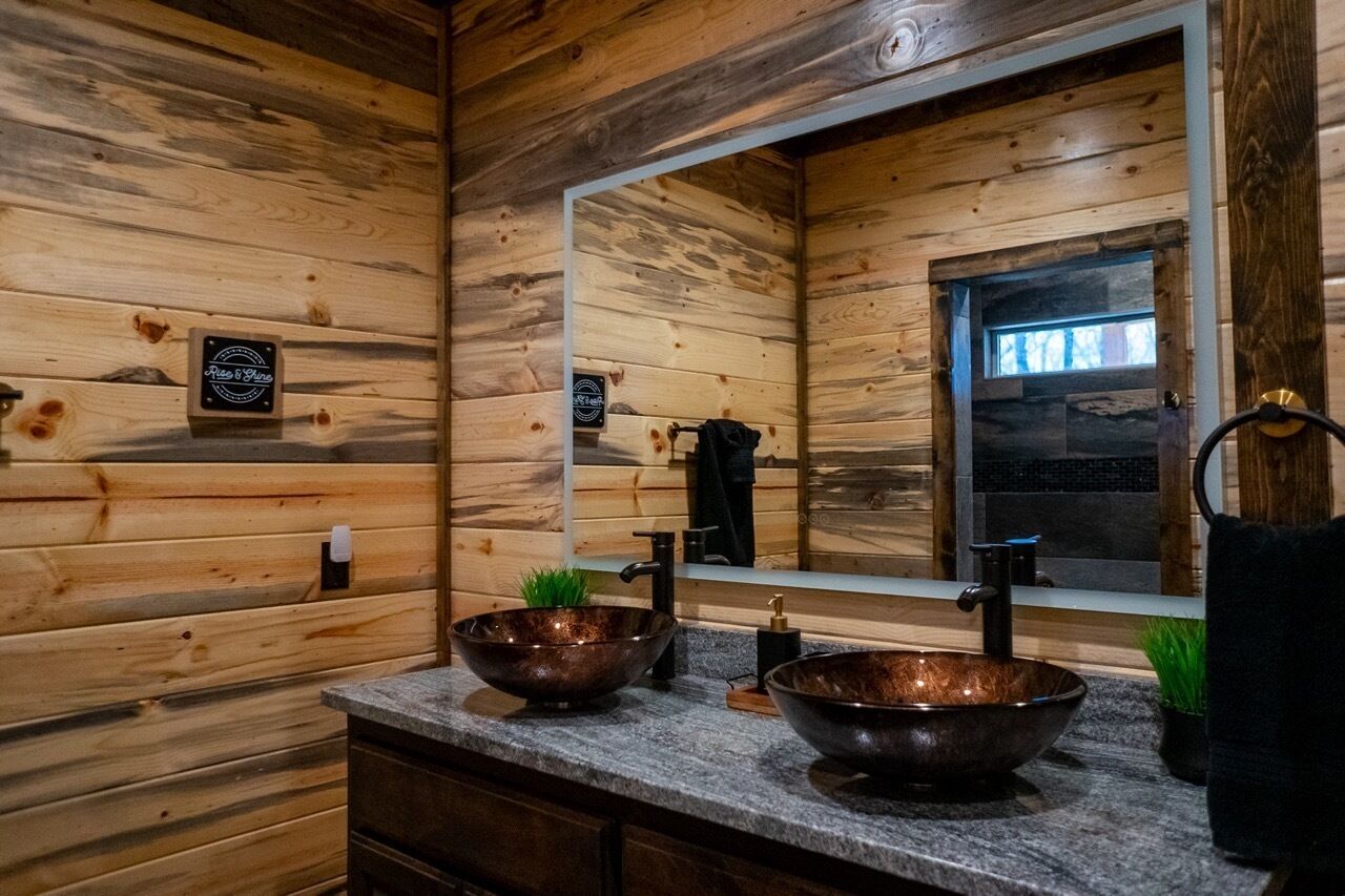 Un baño de cabaña de madera con dos lavabos de cobre, un espejo y una planta pequeña.