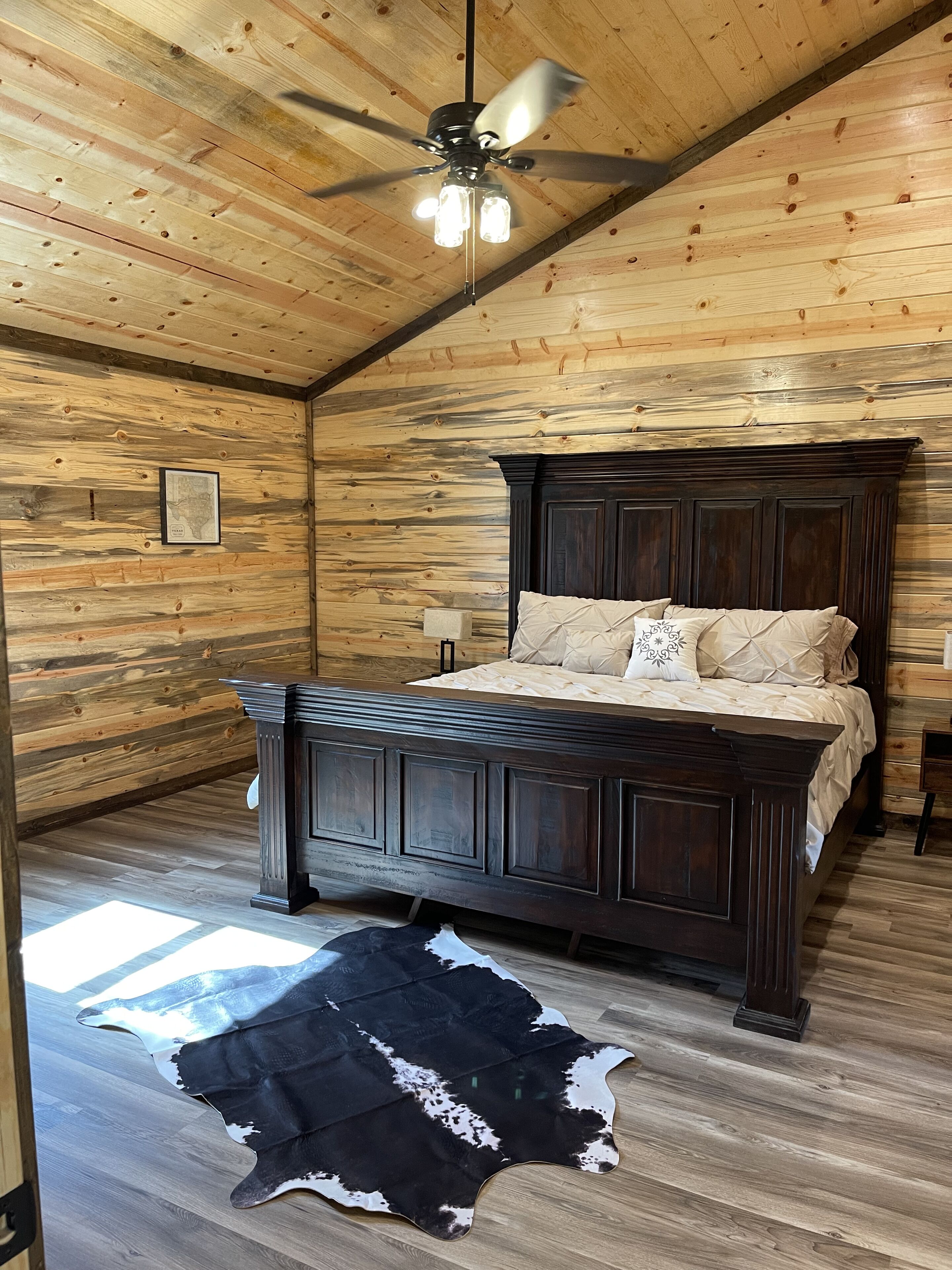 Un dormitorio con techo de madera, una cama de madera oscura, un tapete de cuero de vaca y un ventilador de techo.