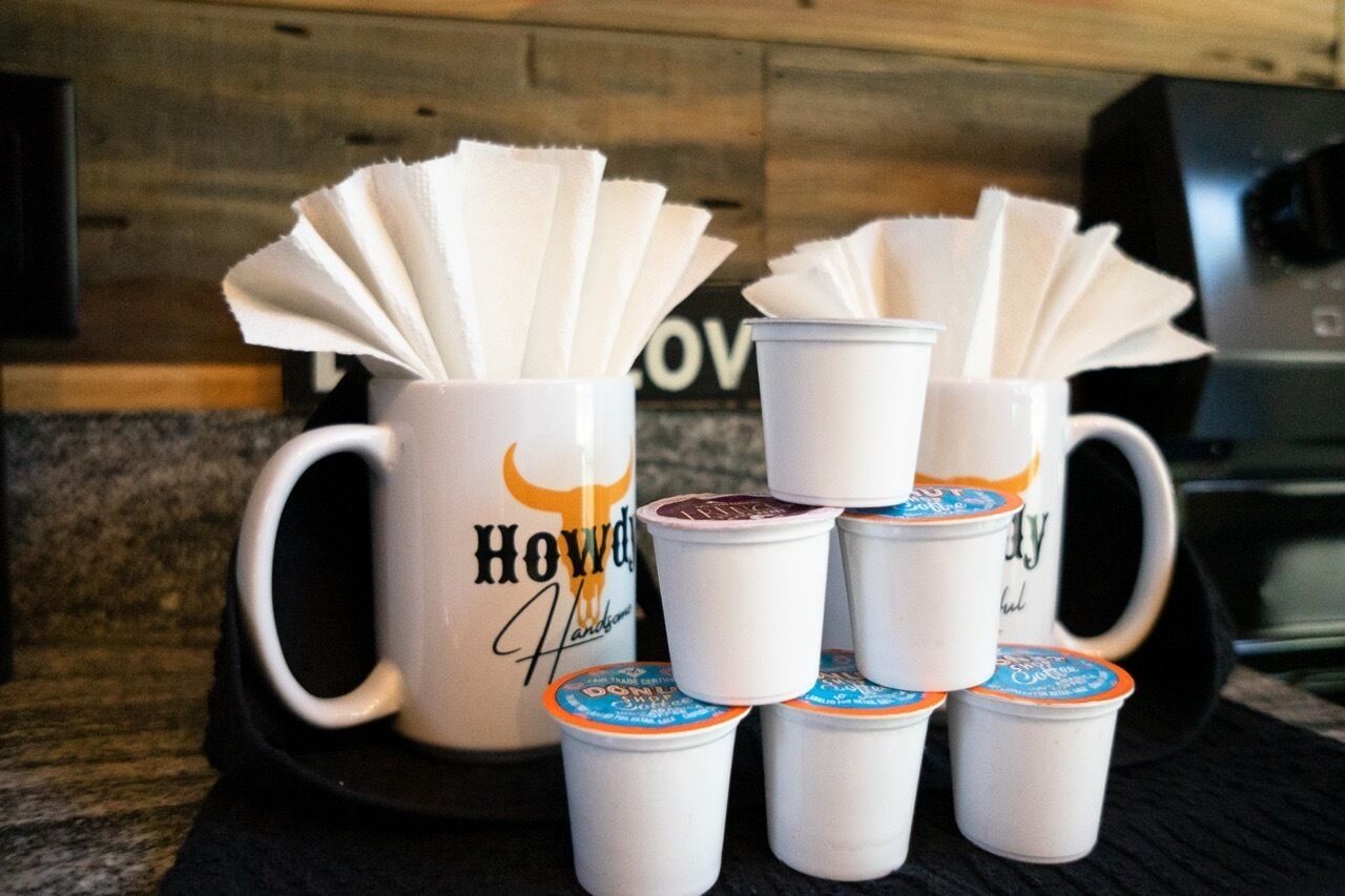 A kitchen counter with a coffee mug and several disposable cups with lids.