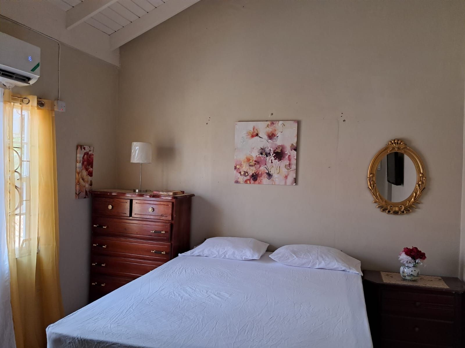 A bedroom with a bed, dresser, wall art, and a mirror.