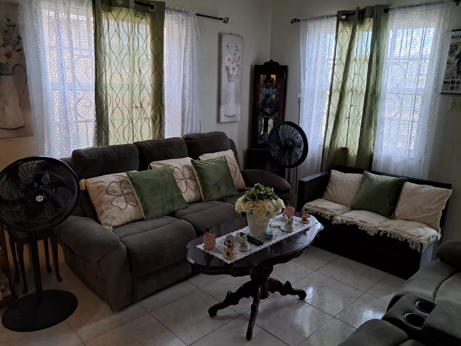 A living room with a sofa, a coffee table with a vase, and two standing fans.