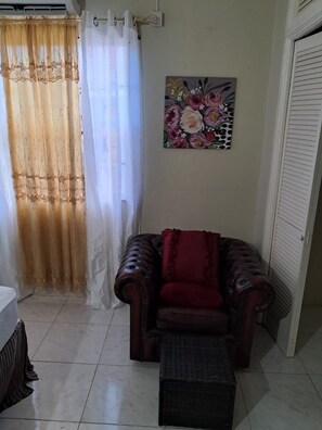 Ein Wohnzimmer mit Ledersofa, einem kleinen Hocker, einem Blumenbild an der Wand und einem halb geöffneten Vorhang.
