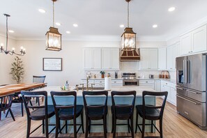 Cocina moderna con armarios blancos, una isla central con taburetes de bar, electrodomésticos de acero inoxidable e iluminación colgante.