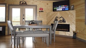 Een houten interieur met een eettafel, stoelen, een open haard en een tv waarop streamingdiensten worden getoond.