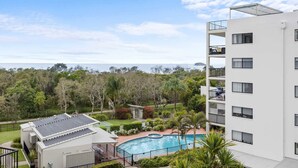 Un immeuble d’appartements moderne doté d’une piscine sur le toit, entouré d’une végétation luxuriante et offrant une vue sur l’océan.