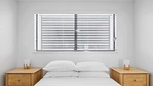 Une chambre à coucher avec un lit, deux tables de chevet en bois et une fenêtre avec des stores.