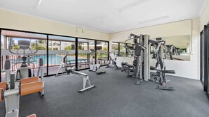 Une salle de sport équipée de divers appareils d’exercice, dotée de grandes fenêtres et offrant une vue sur une piscine.