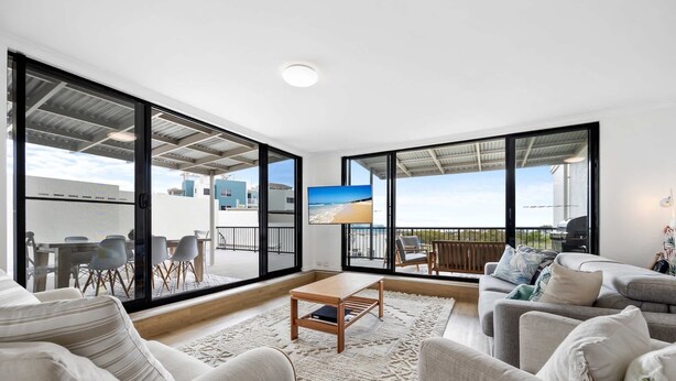 Un vaste espace de vie doté de grandes fenêtres, d’un téléviseur à écran plat et d’un balcon avec coin salon extérieur.