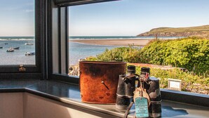 Une fenêtre donnant sur la mer, un seau rouillé et deux appareils photo posés sur une étagère.