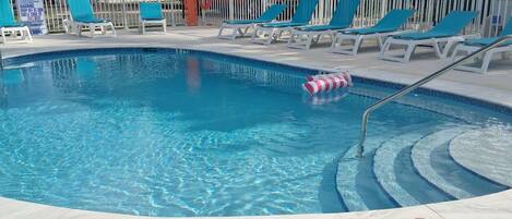 A swimming pool with blue water, surrounded by white lounge chairs and a white fence.
